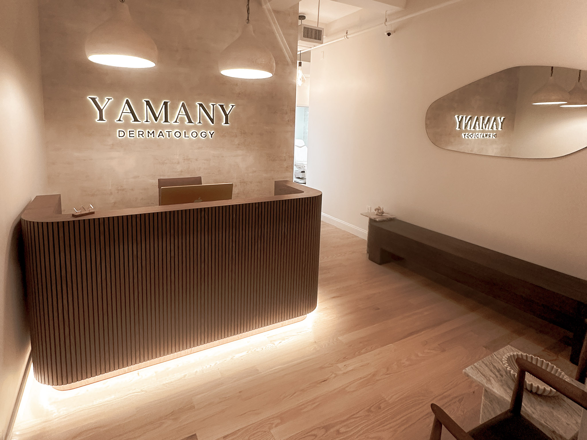 Yamany Dermatology reception area with curved wooden desk and warm, modern design